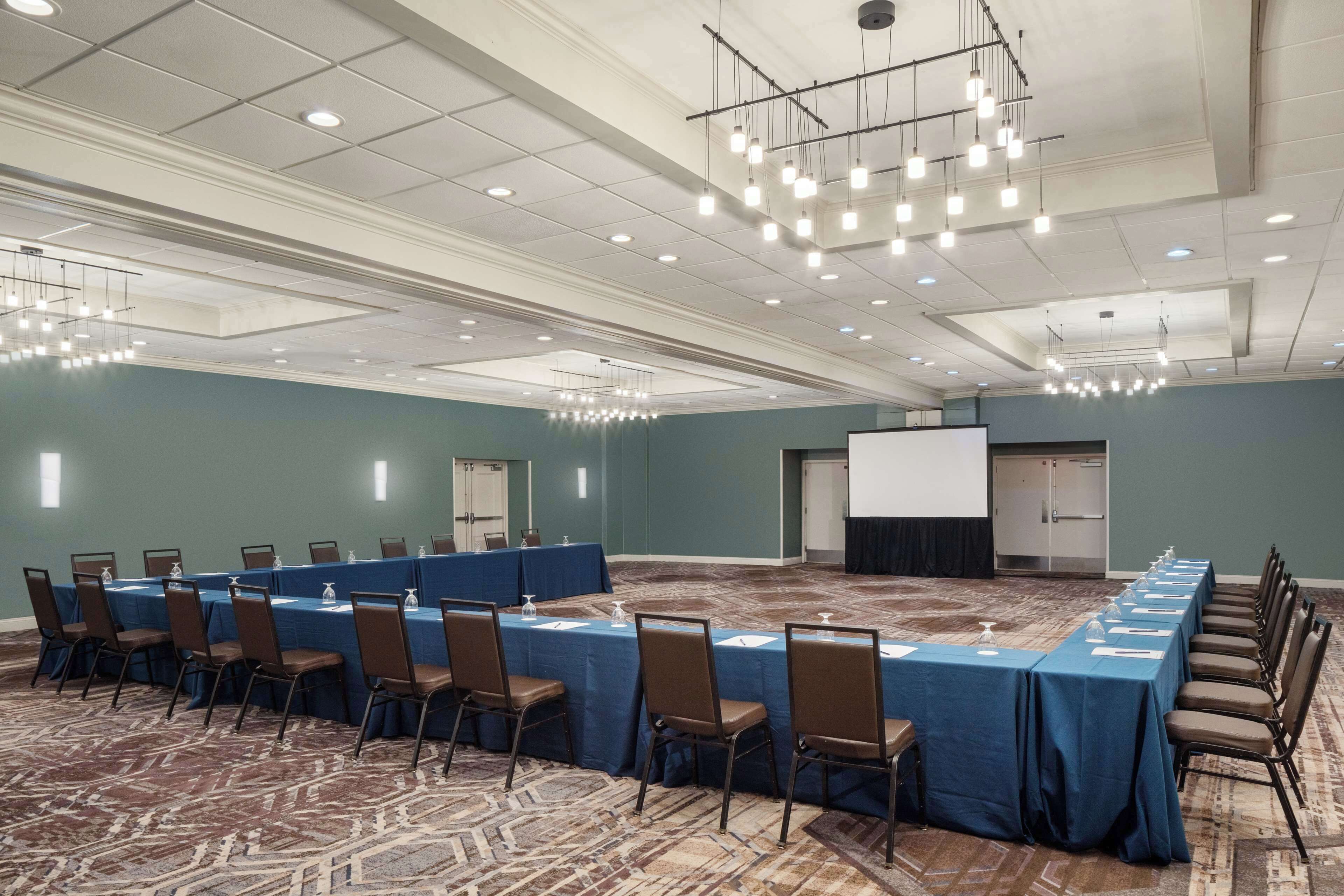 A conference room with a long table, chairs, a projector screen, and a carpeted floor.