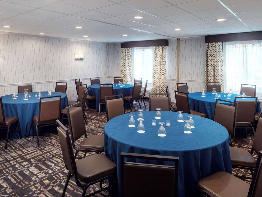 A conference room with round tables covered with blue tablecloths, brown chairs, and glassware on each table.