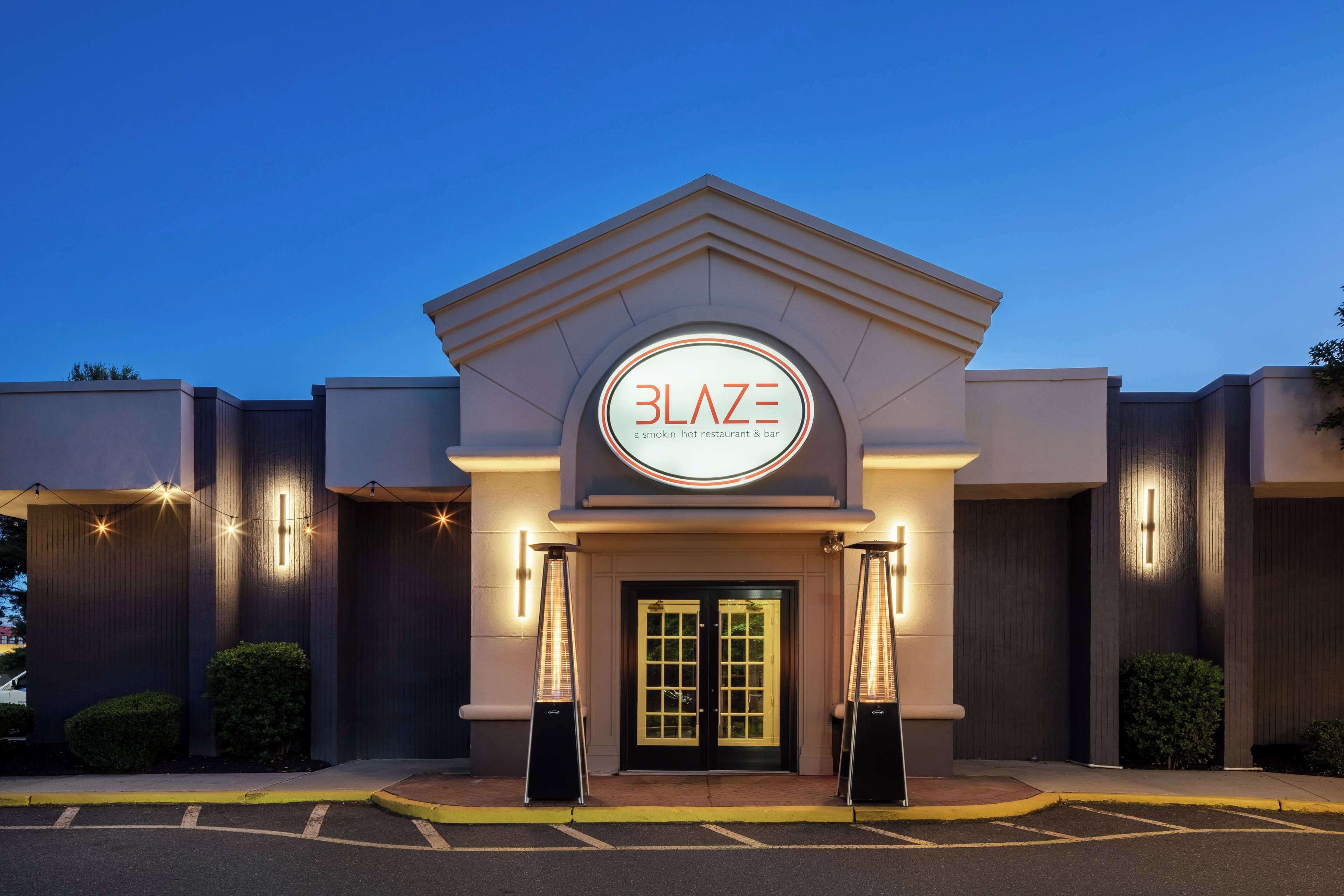 The exterior of a Blaze restaurant and bar with a modern design, featuring a prominent illuminated sign and a gated entrance.