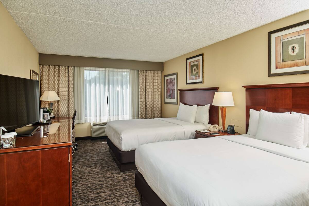 A hotel room with two beds, a desk with a TV, a telephone, and a framed picture on the wall.