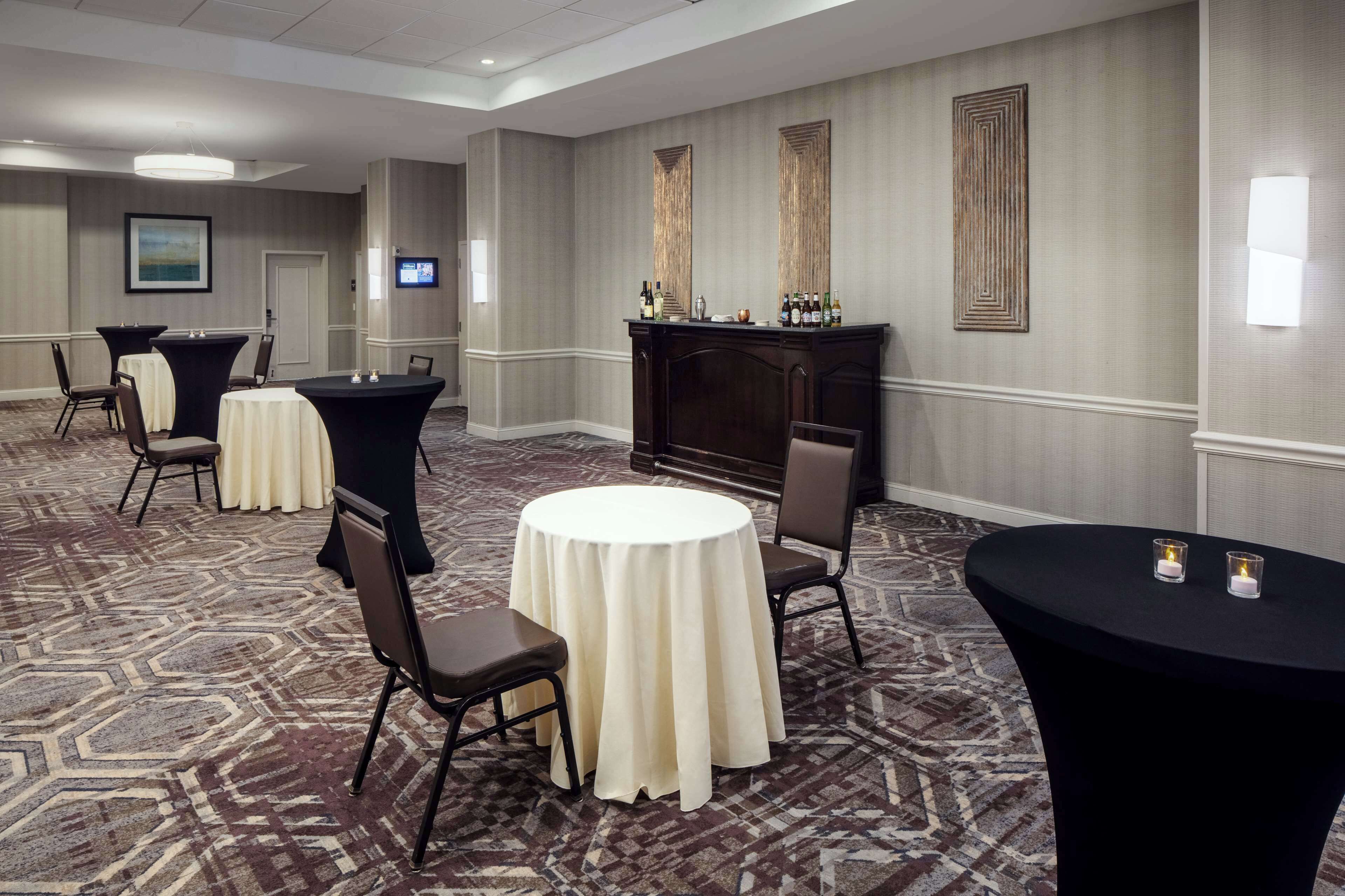 A conference room with round tables, chairs, a bar area, and a television screen.