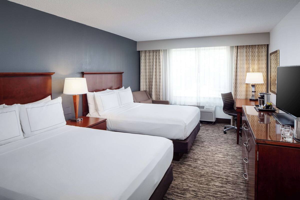 A hotel room with two beds, a desk with a TV, a chair, and a window with curtains.