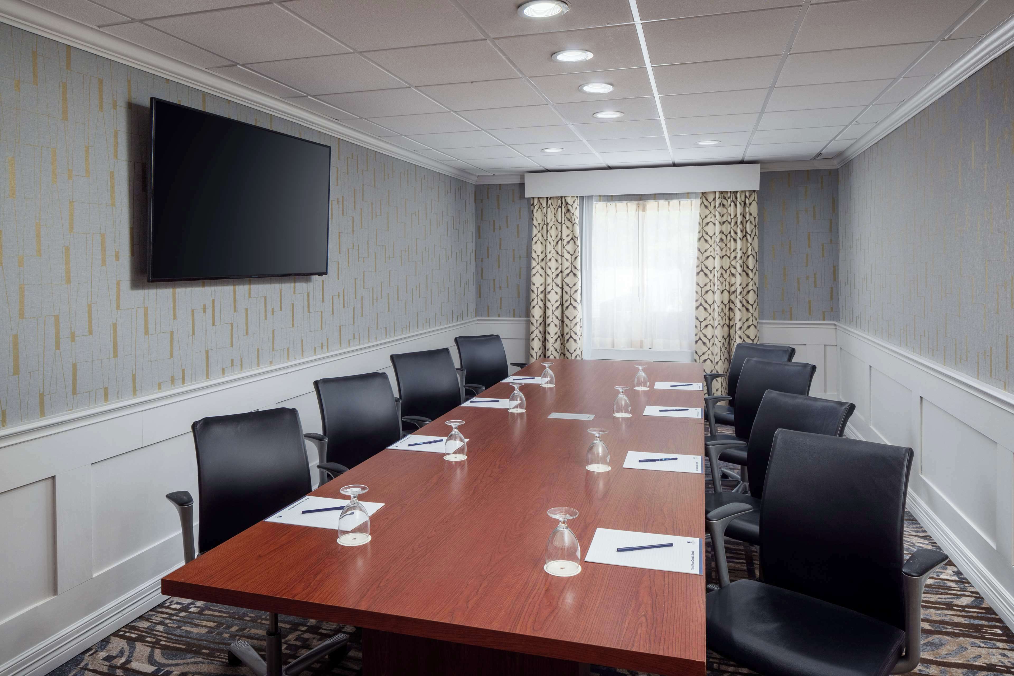 A conference room with a long table, black chairs, and a flat-screen TV on the wall.