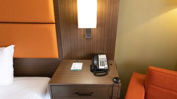 Una habitación de hotel con una mesita de noche de madera, un teléfono, una libreta y una silla.