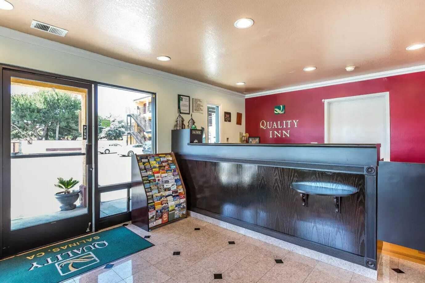 A reception area with a red wall, a reception desk, a window with a view of the street, and a sign for the Quality Inn.