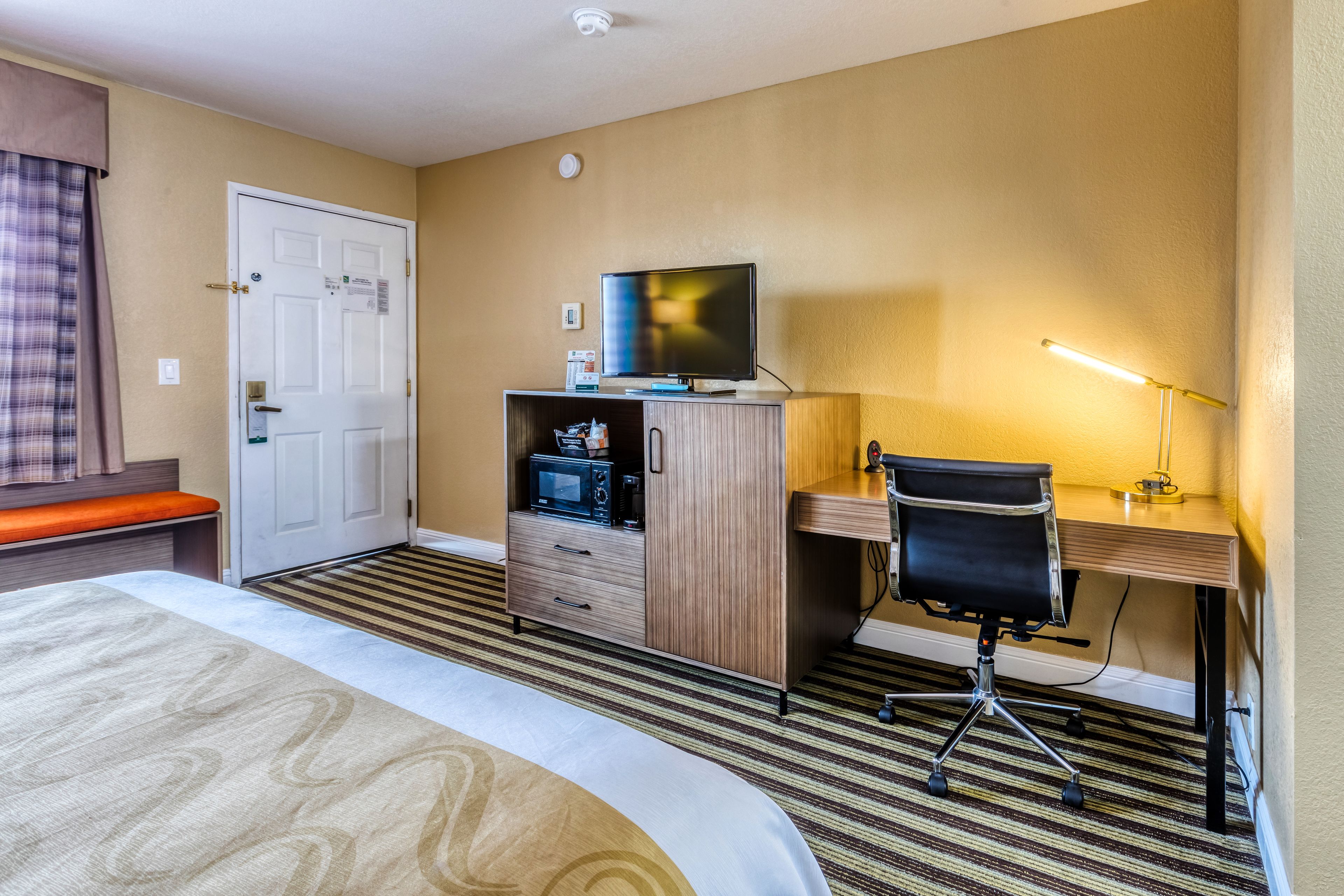 Ein Hotelzimmer mit einem Bett, einem Schreibtisch mit Computer und Stuhl, einem Fernseher und einer Minibar.