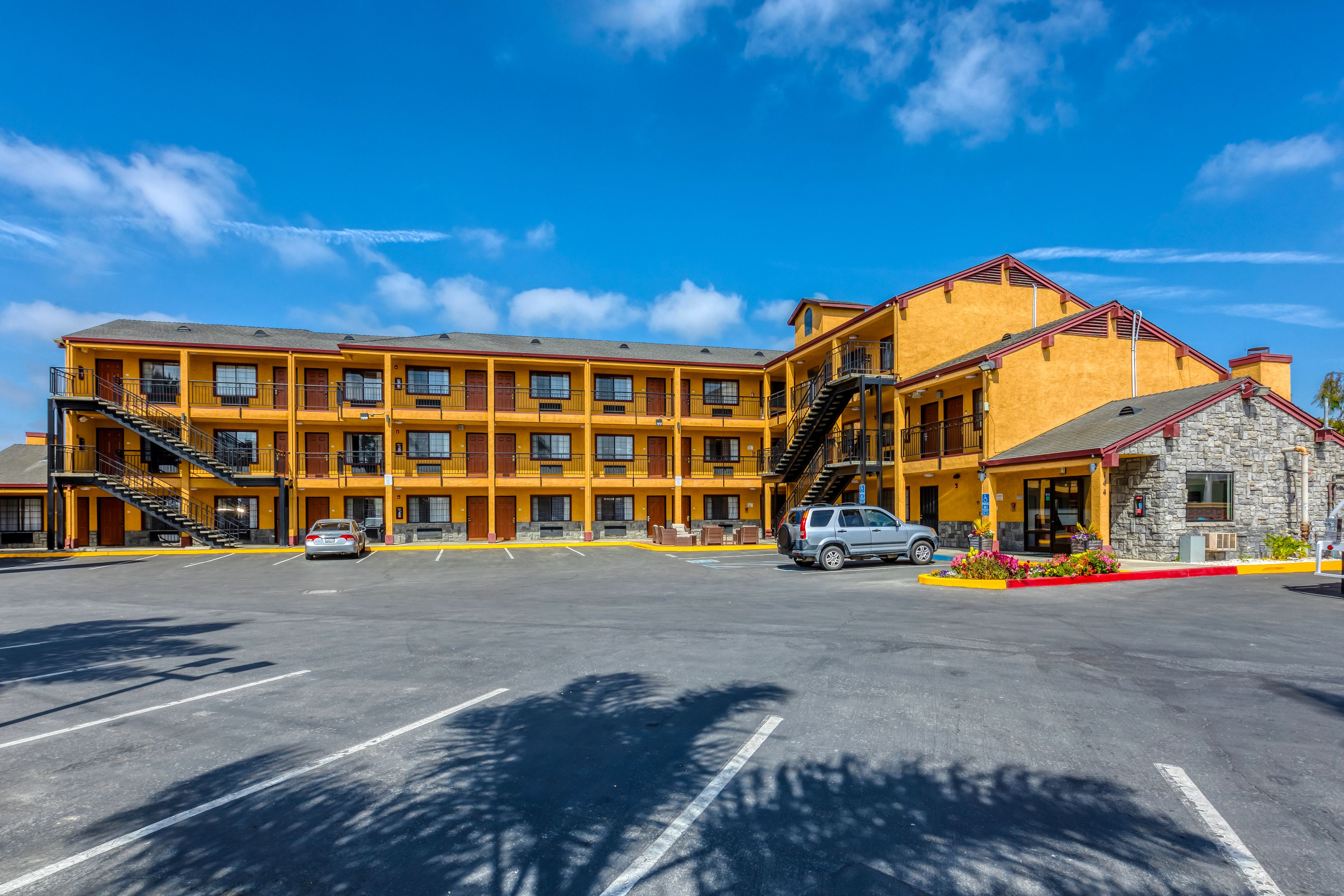 A multi-story hotel with a yellow facade, multiple balconies, and a parking lot.