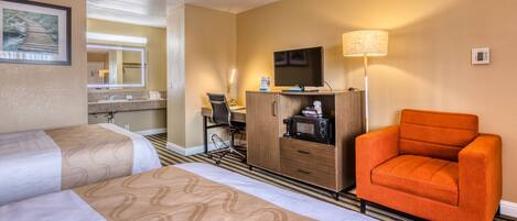 A hotel room with two beds, a desk with a chair, a television, a microwave, and a lamp.