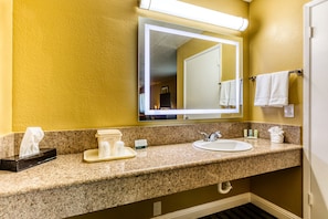 Baño de hotel con encimera de granito, lavamanos, espejo y toallas en un perchero.