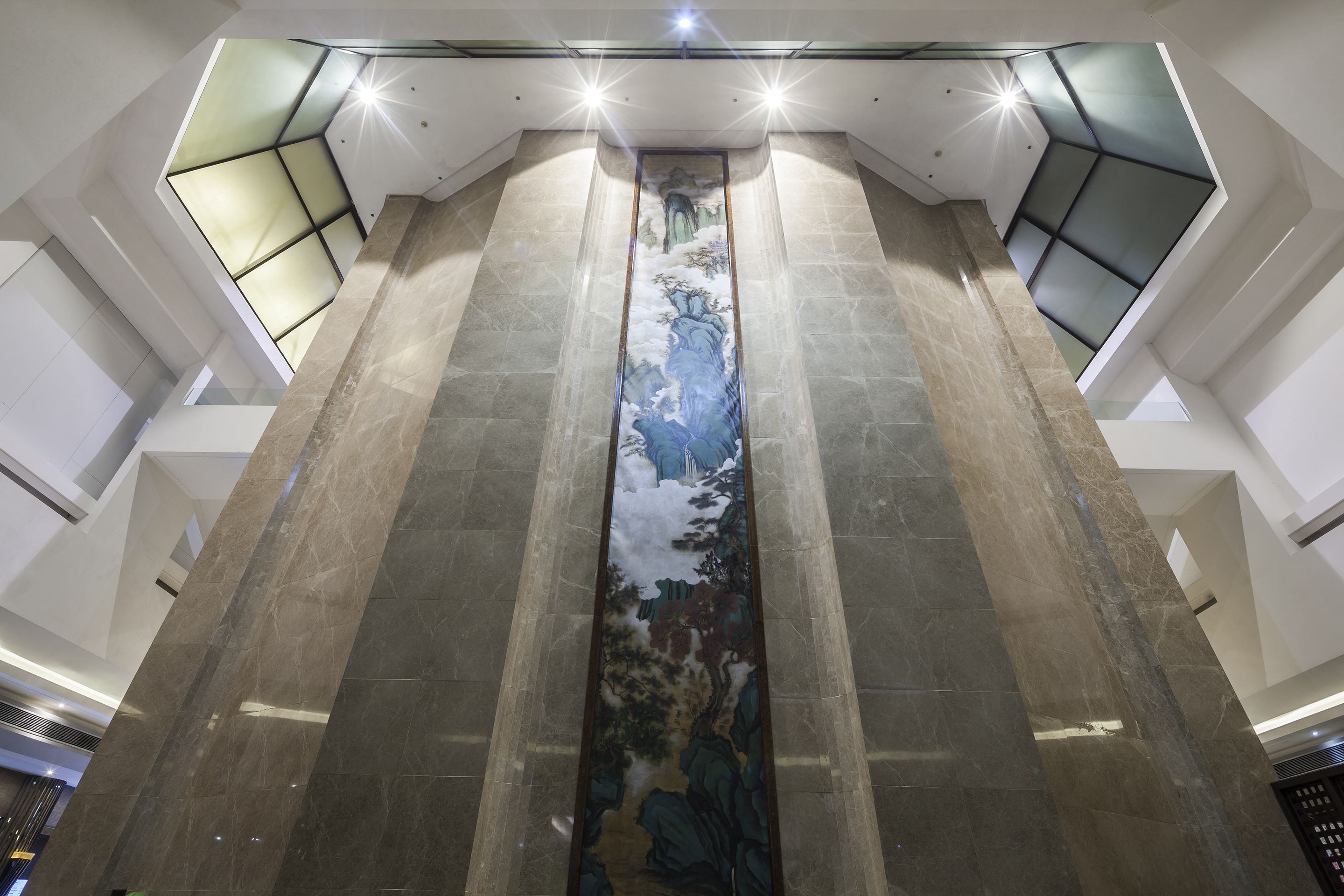 A modern interior with a central column featuring a detailed mural, high ceilings, and contemporary lighting fixtures.