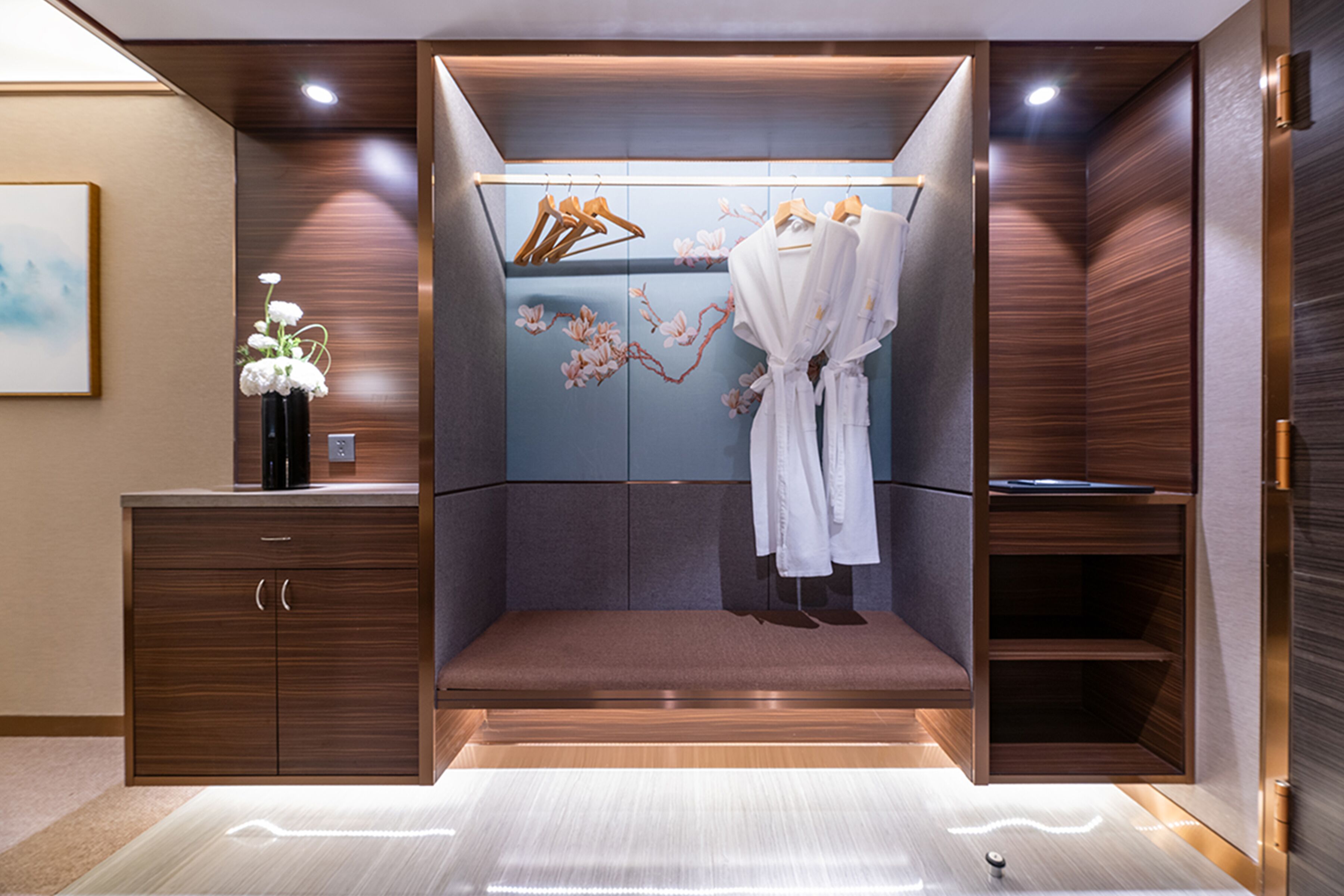 A modern, enclosed walk-in closet with wooden cabinetry, a bench, and a hanging robe rack.
