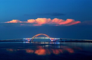 Un puente con arcos iluminados que se reflejan en aguas tranquilas.