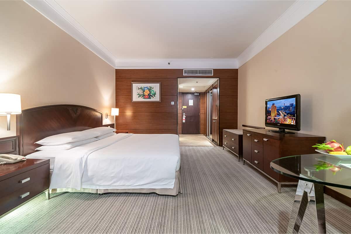 Ein Hotelzimmer mit einem Bett, einem Schreibtisch mit Fernseher, einem Schminktisch und Teppichboden.