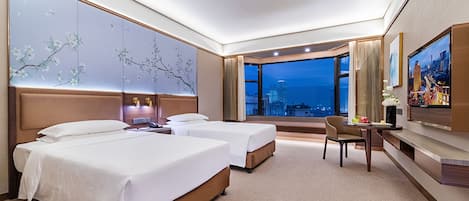 A hotel room with two beds, a desk, a chair, a TV, and a large window with a city view.