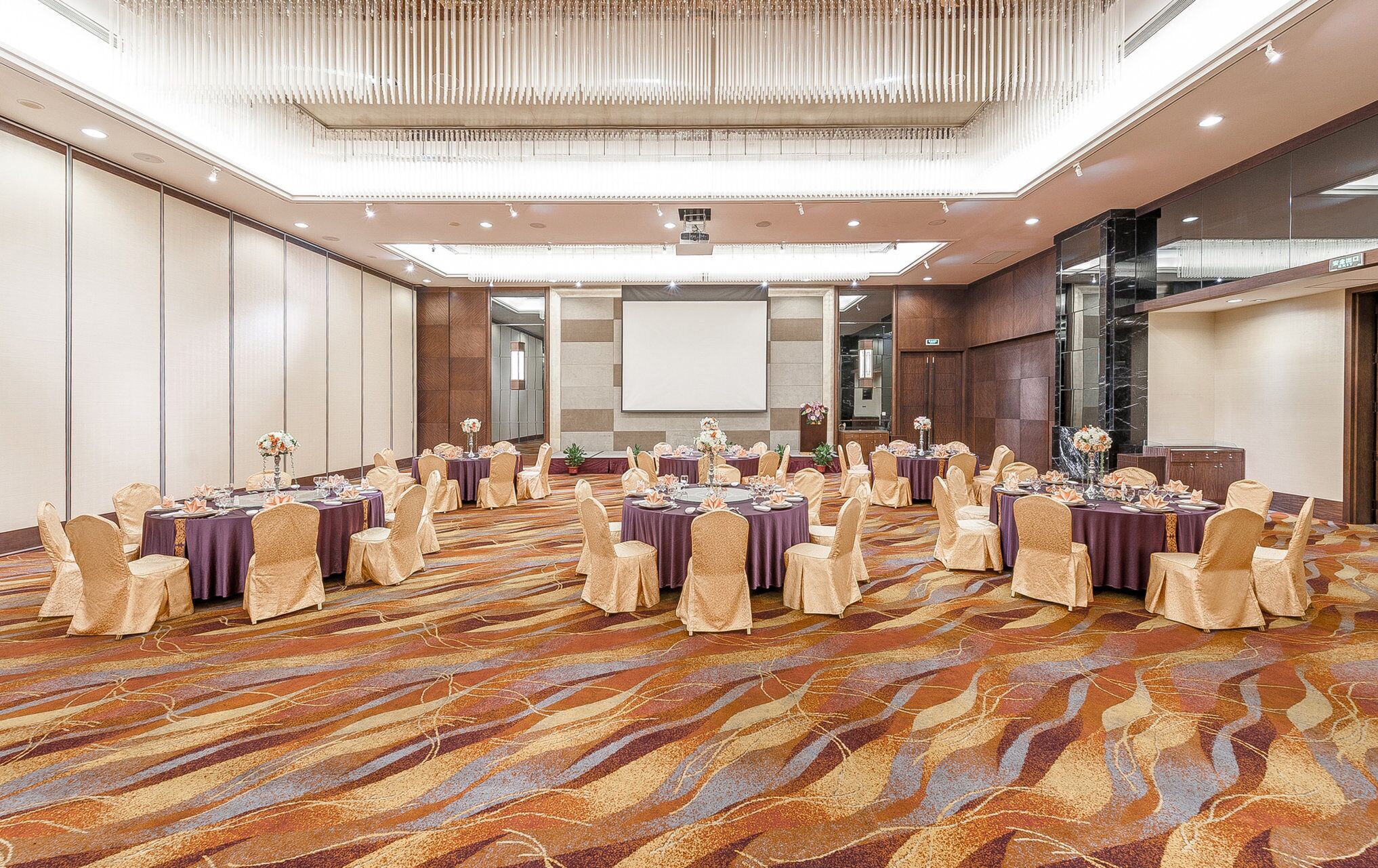 A conference room with round tables, chairs, and a large screen.