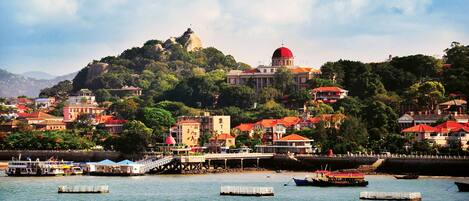 A coastal town with a prominent hilltop building, a bridge, and several boats on the water.