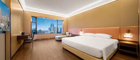 A modern hotel room with a large bed, a desk, and a view of a cityscape through a large window.