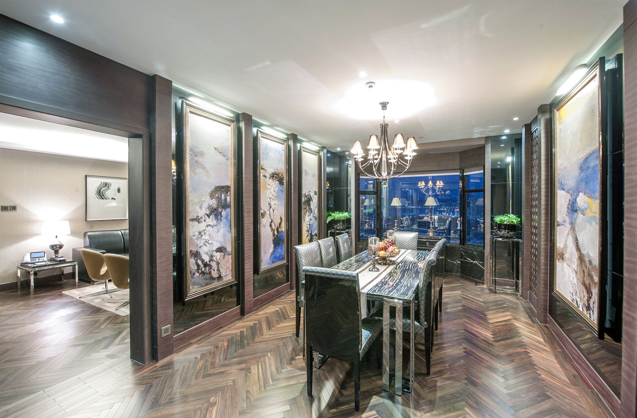 A dining area with a herringbone floor, a chandelier, and artwork on the walls.