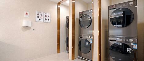 A laundry facility with three stacked washers and dryers, a wall-mounted air purifier, and informational posters on the wall.
