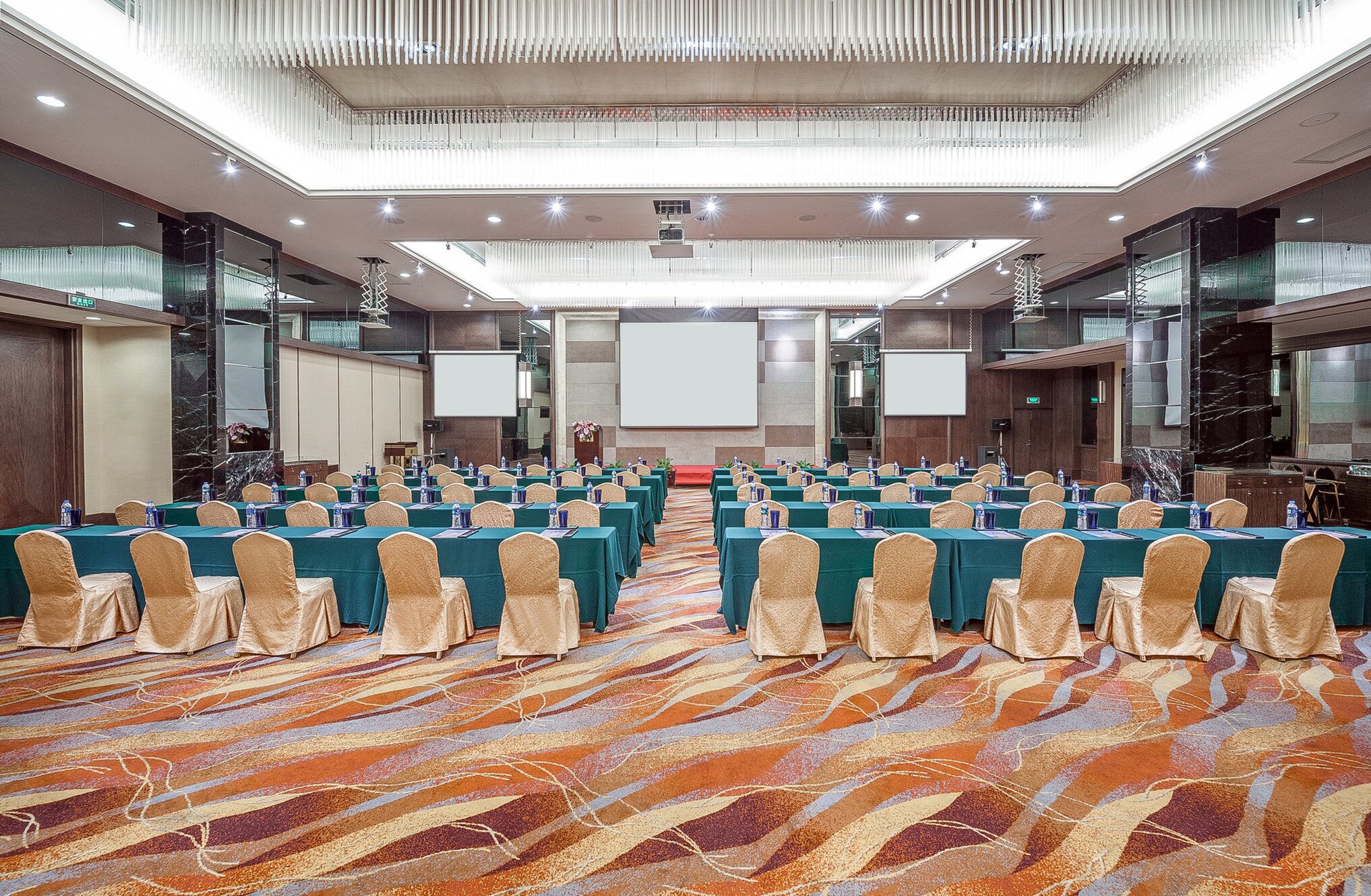 A conference room with rows of tables and chairs, a large screen, and a carpeted floor.