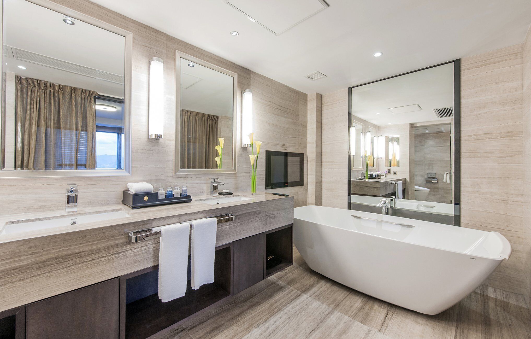 A modern bathroom with a large freestanding bathtub, a vanity with a mirror, and a television.