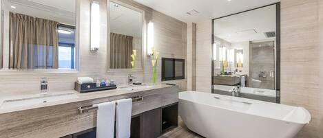 A modern bathroom with a large freestanding bathtub, a vanity with a mirror, and a television.