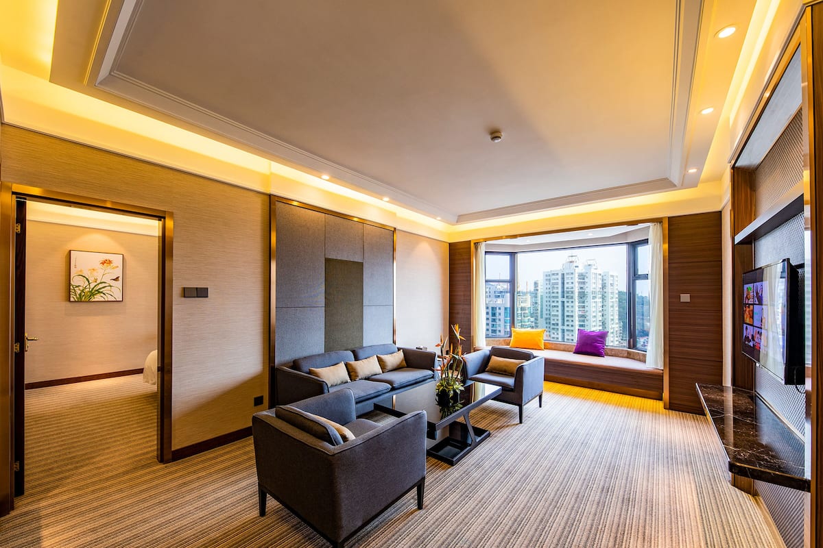 Ein modernes Hotelzimmer mit einer Sofagarnitur, einem Couchtisch und einem großen Fenster mit Blick auf die Stadt.