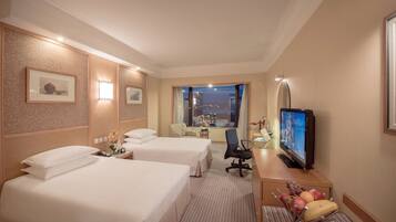 A hotel room with two beds, a desk with a television, a chair, and a window with a city view.
