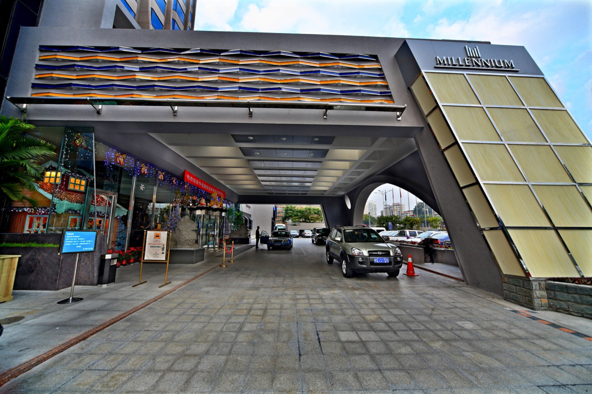 The entrance to the Hilton Millennium hotel with a modern design, including a distinctive roof structure and a sign indicating the hotel's name.