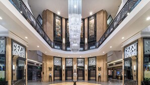 Eine großzügige Lobby mit einem zentralen Kronleuchter, mehreren Aufzügen und einem Marmorboden.