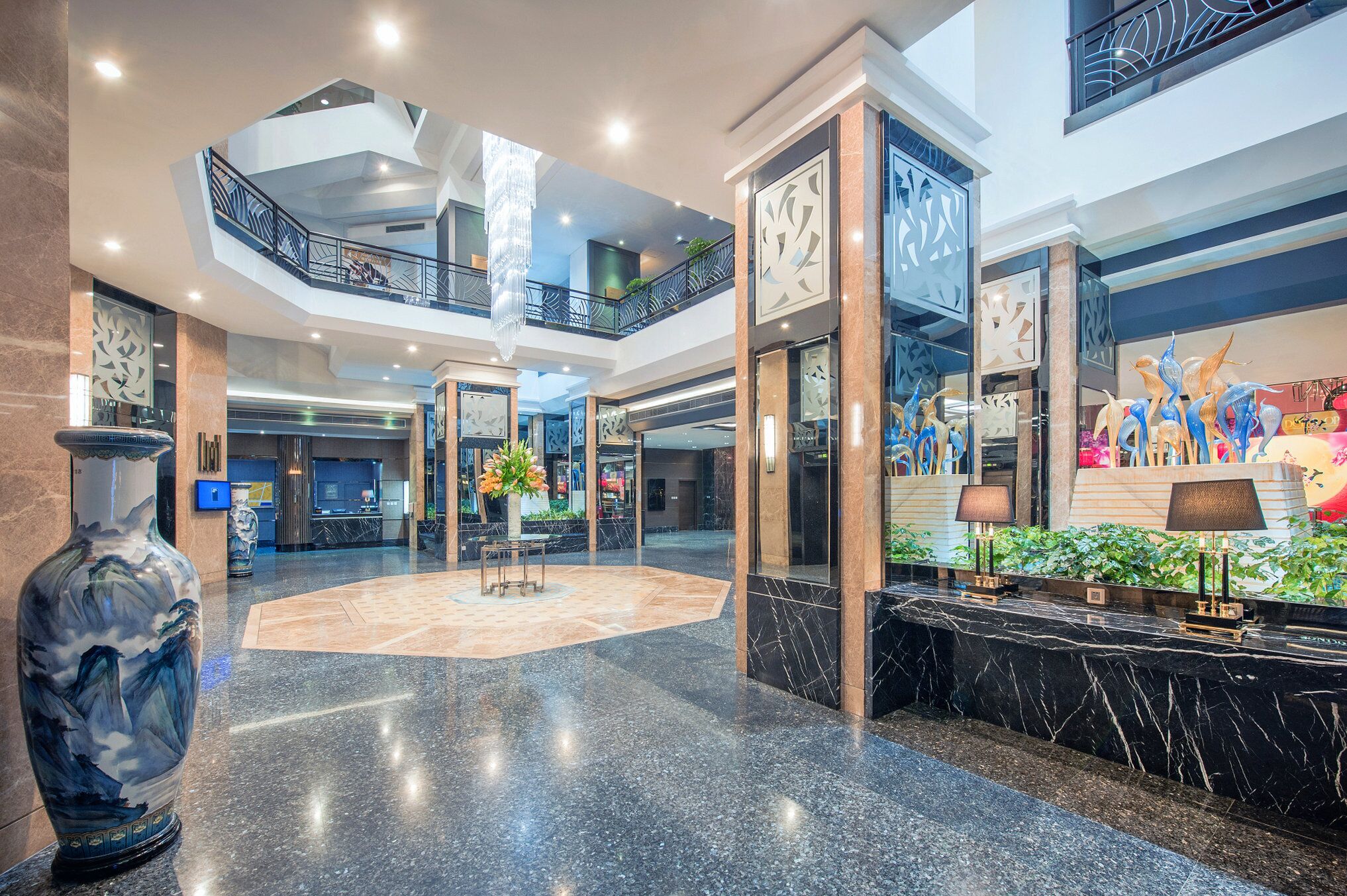 A spacious lobby with a marble floor, a large vase, and a reception desk with lamps.