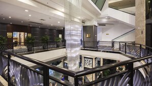 Een meerlaagse atriumruimte met een centrale glazen kolom, meerdere verdiepingen en een moderne trap.