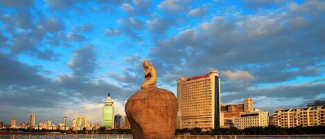 A large stone sculpture in a body of water with a city skyline in the background.