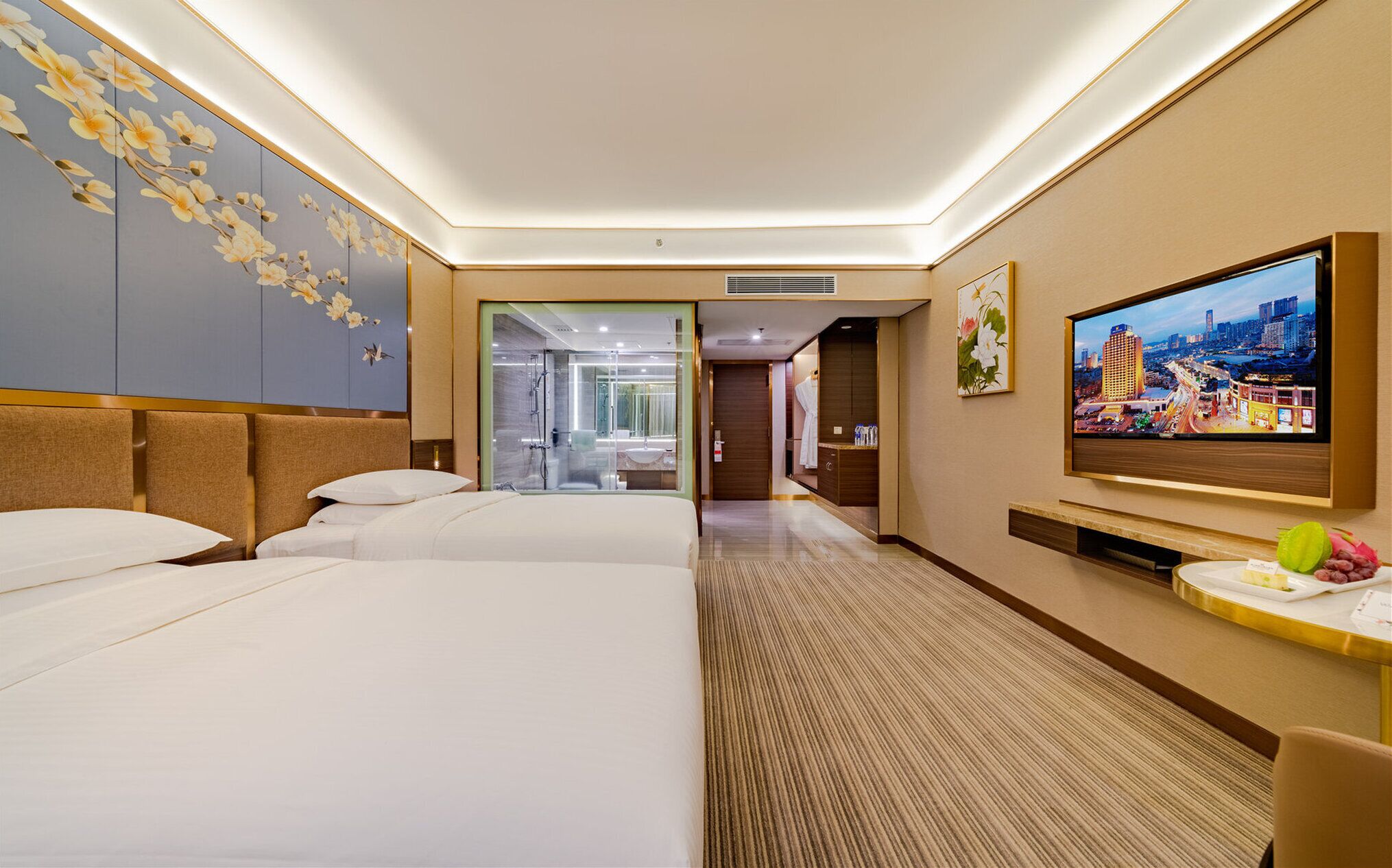 A hotel room with two beds, a TV, and a bathroom visible through a glass door.