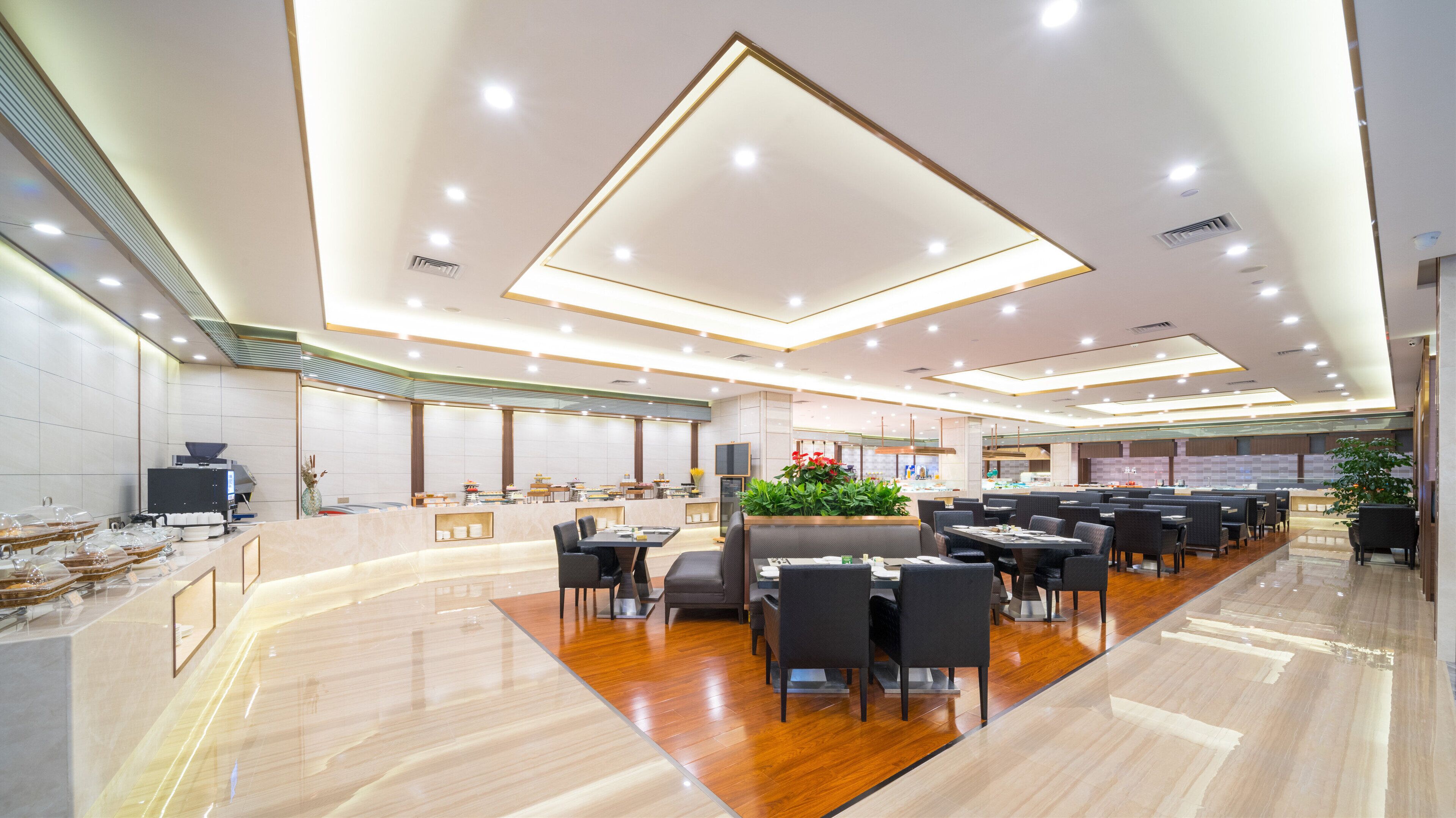 Ein geräumiges Restaurant mit modernem Design, das einen zentralen Sitzbereich mit Tischen und Stühlen, eine Theke mit Kasse und eine Küchenzeile im Hintergrund bietet.