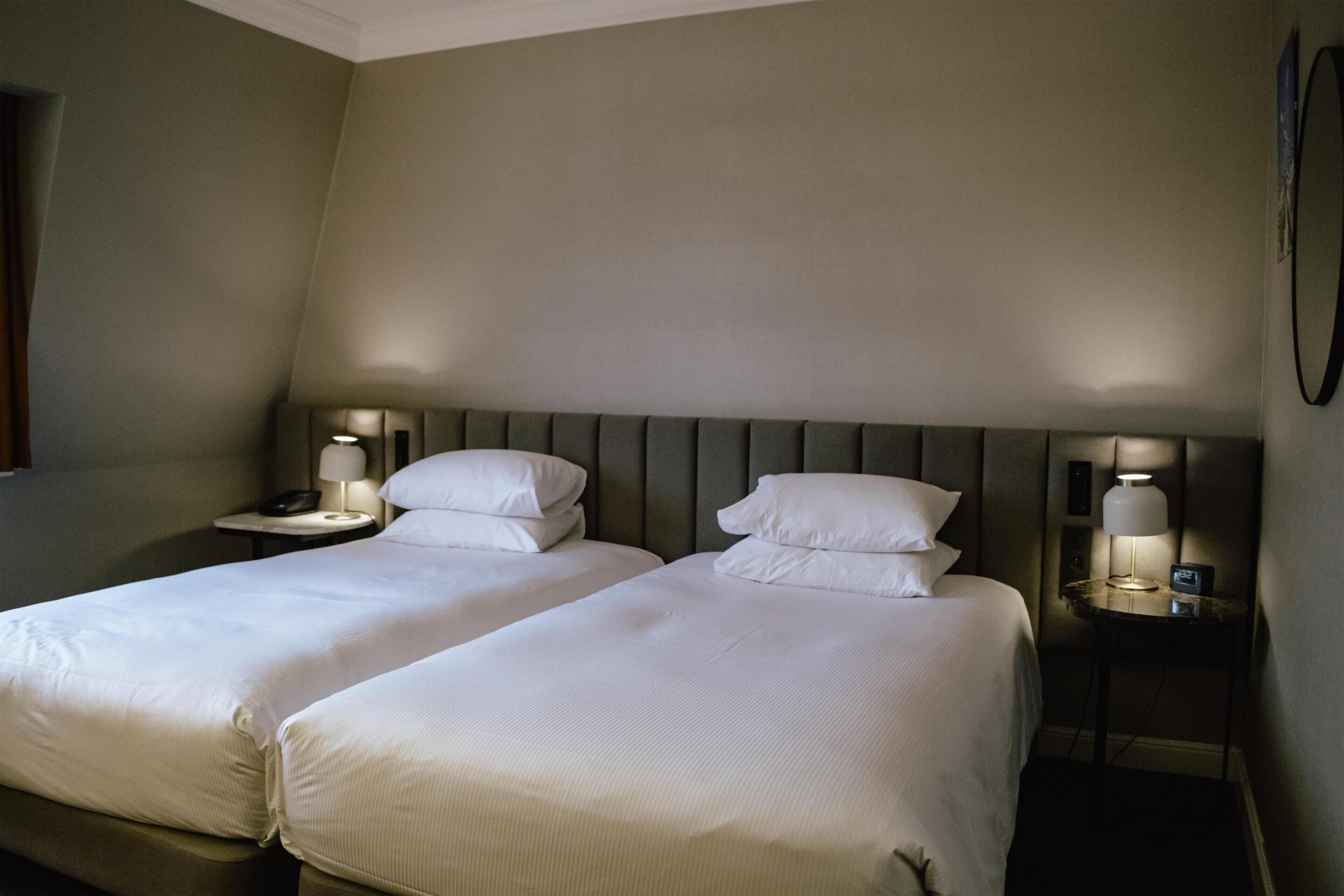 A hotel room with two beds, each with a pillow and a nightstand with a lamp.