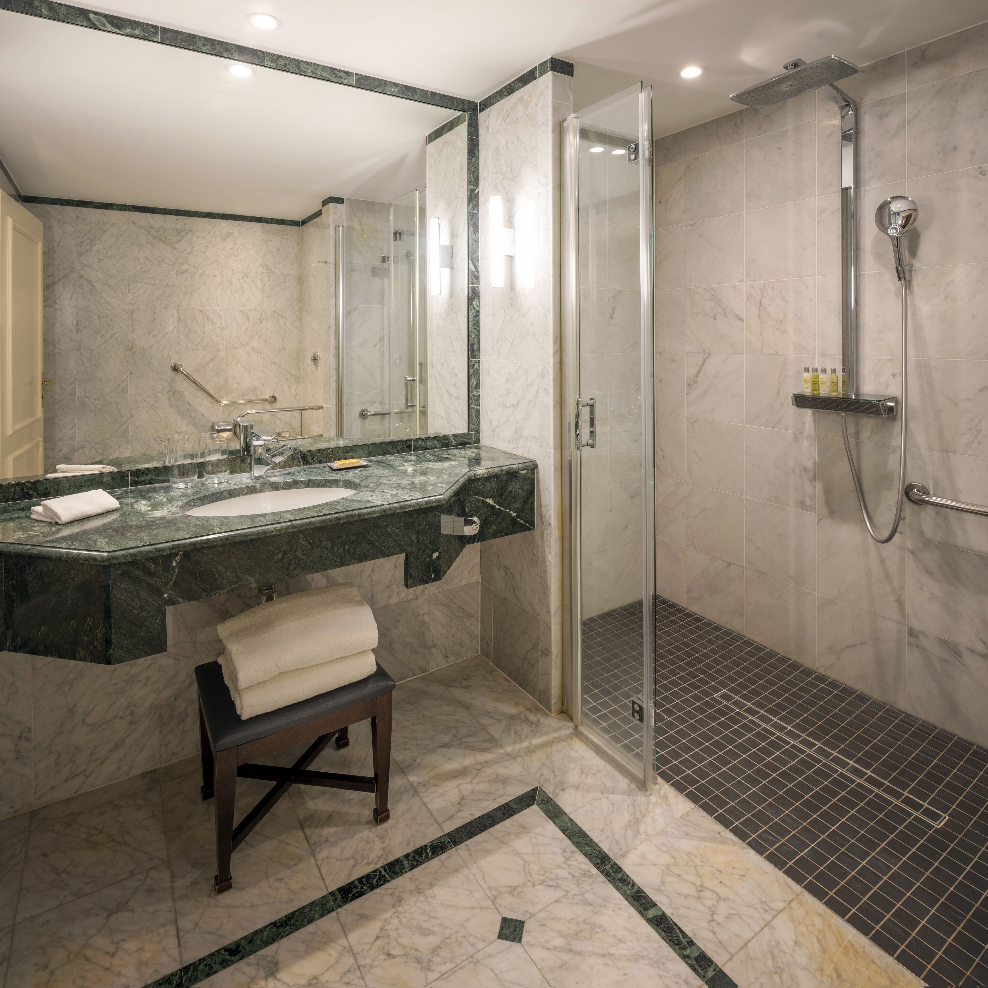 A modern bathroom with a glass shower enclosure, a marble sink, and a bench.