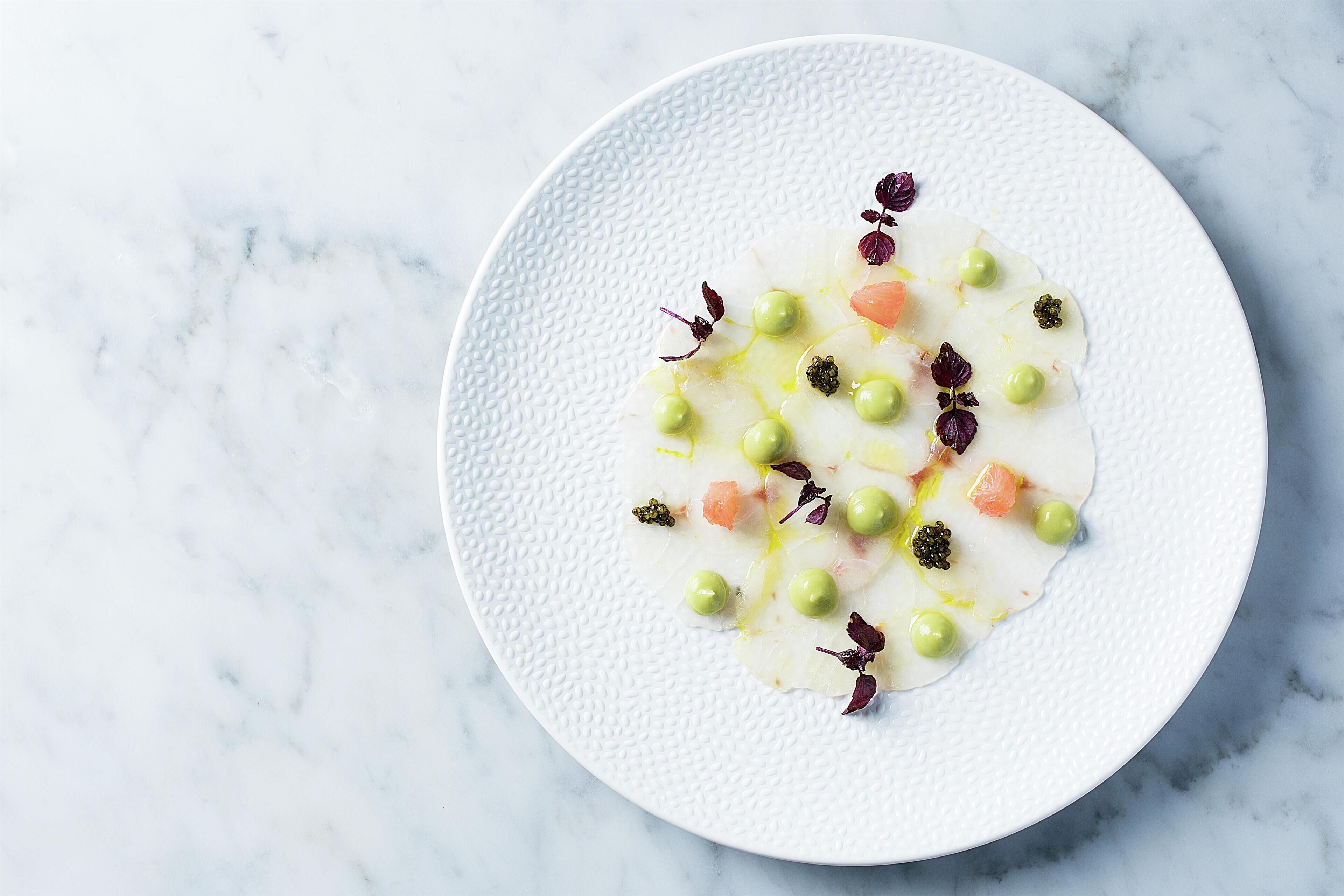 Un plato blanco con textura y un postre blanco sobre una superficie de mármol.