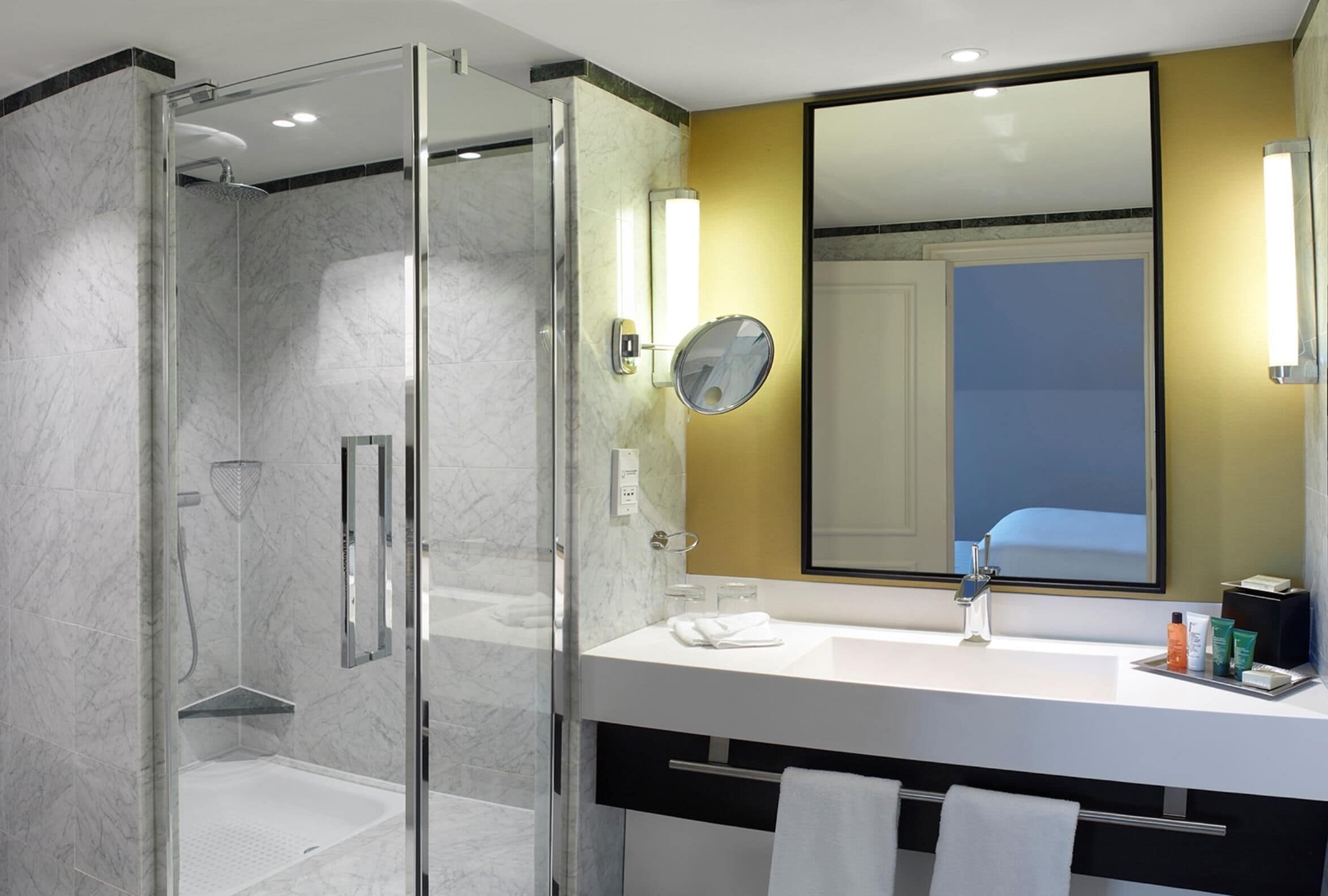 A modern bathroom with a glass-enclosed shower, a white sink, and a large mirror.