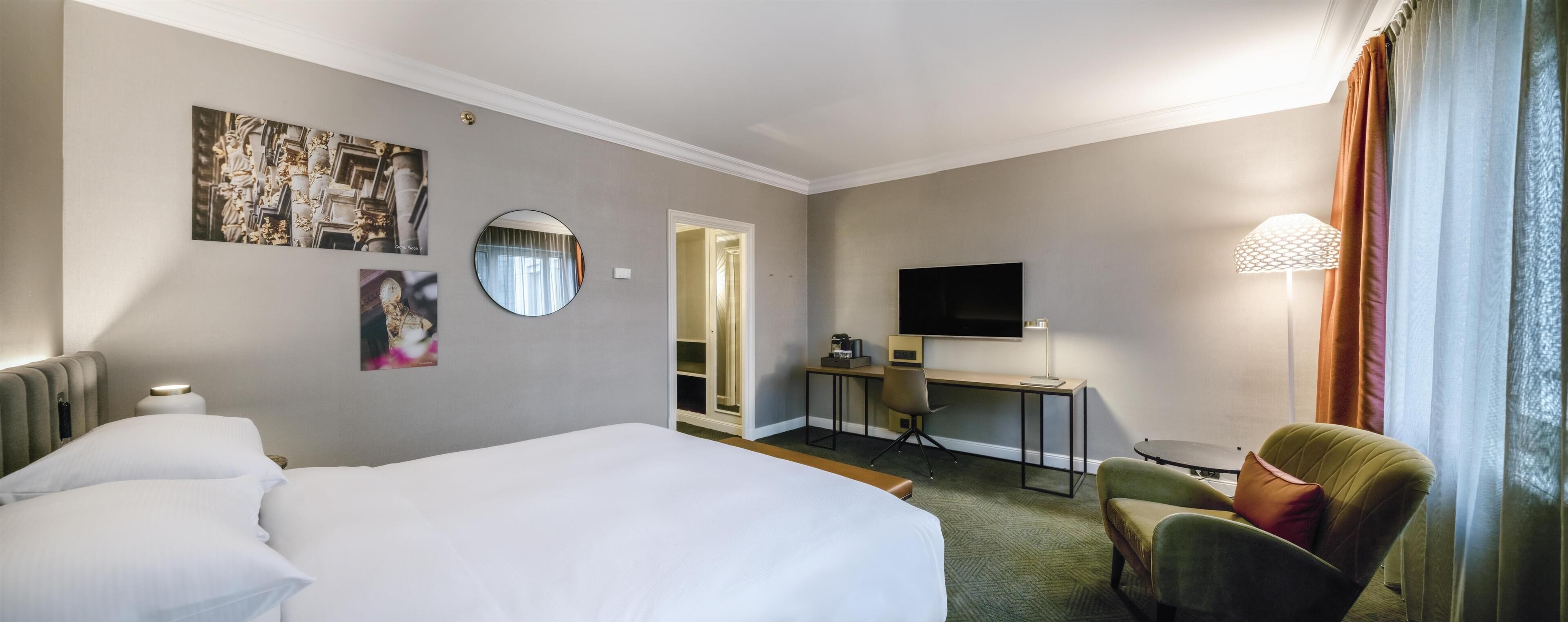 Habitación de hotel con cama, escritorio, silla, televisor y lámpara.