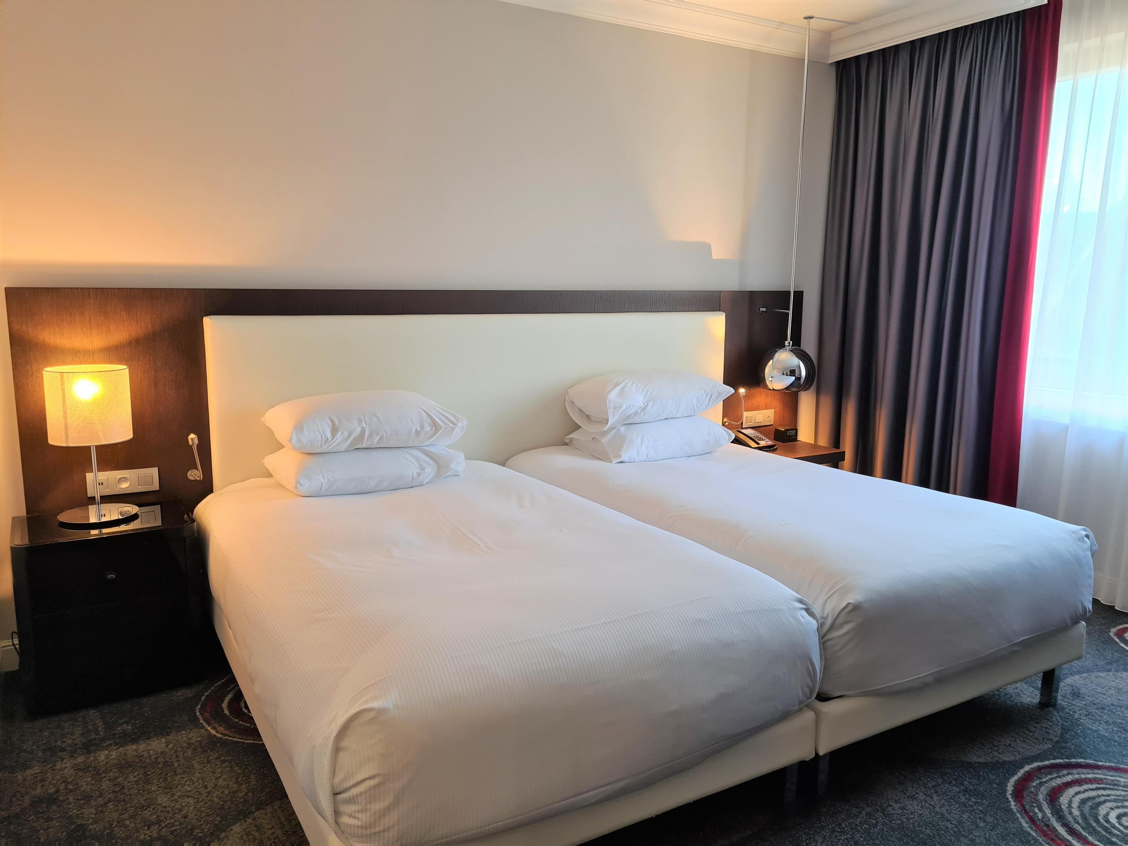 Et hotelværelse med to senge, et natbord med lampe, telefon og spejl.
