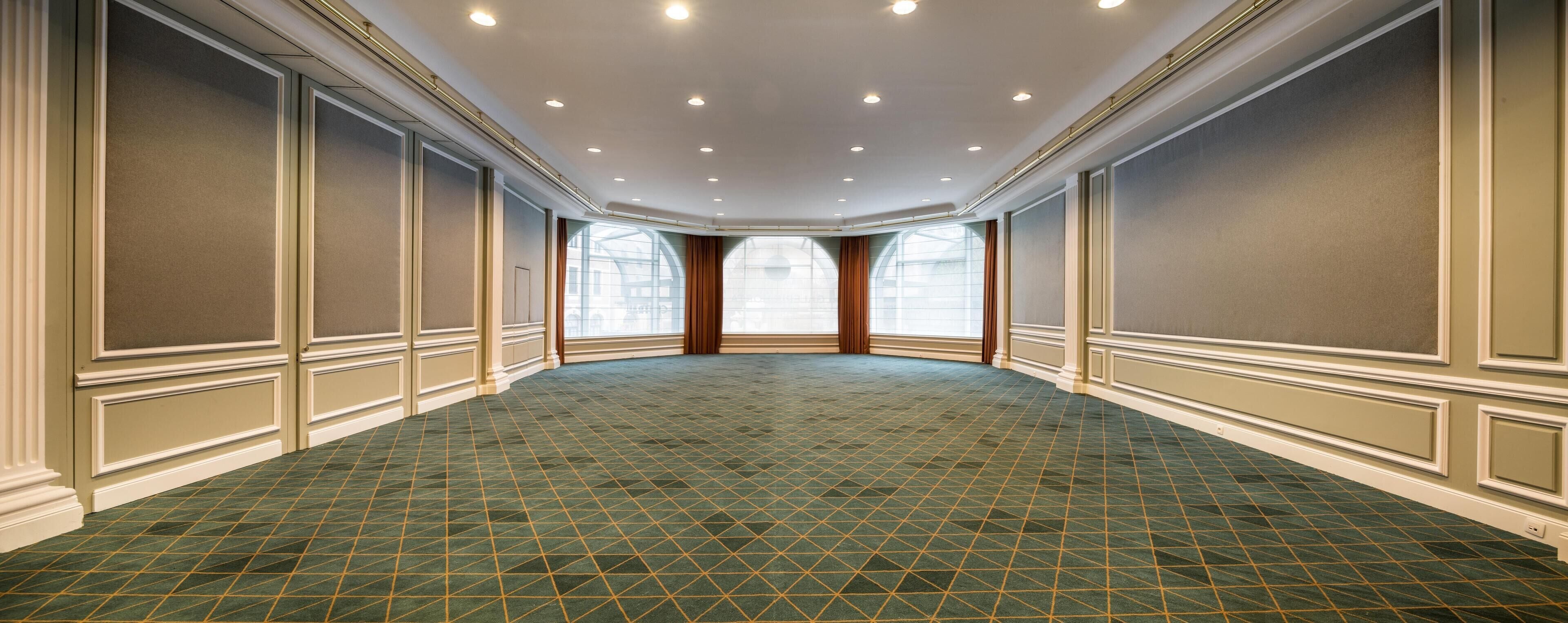 Una amplia y luminosa sala de conferencias con alfombra de diseño verde, ventanas grandes con cortinas y un techo alto con iluminación empotrada.