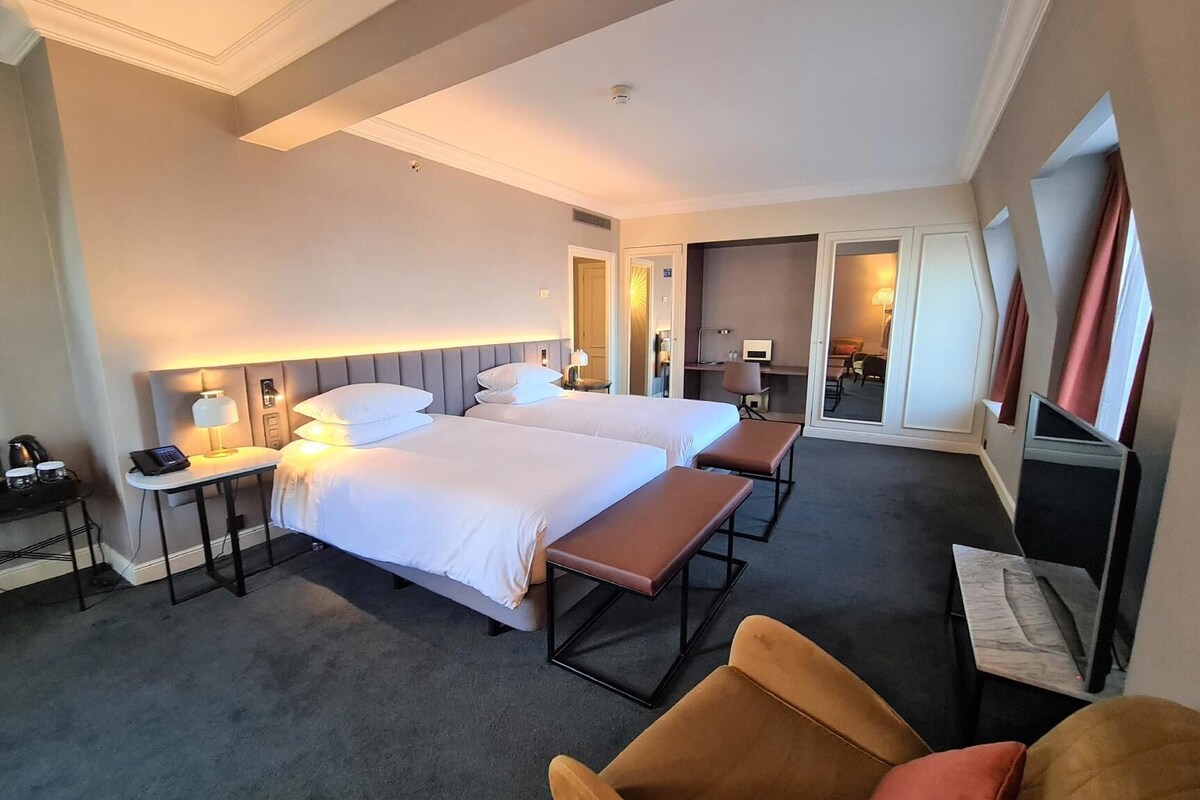 Ett hotellrum med två sängar, ett skrivbord med en telefon och en lampa, en stol och en tv.