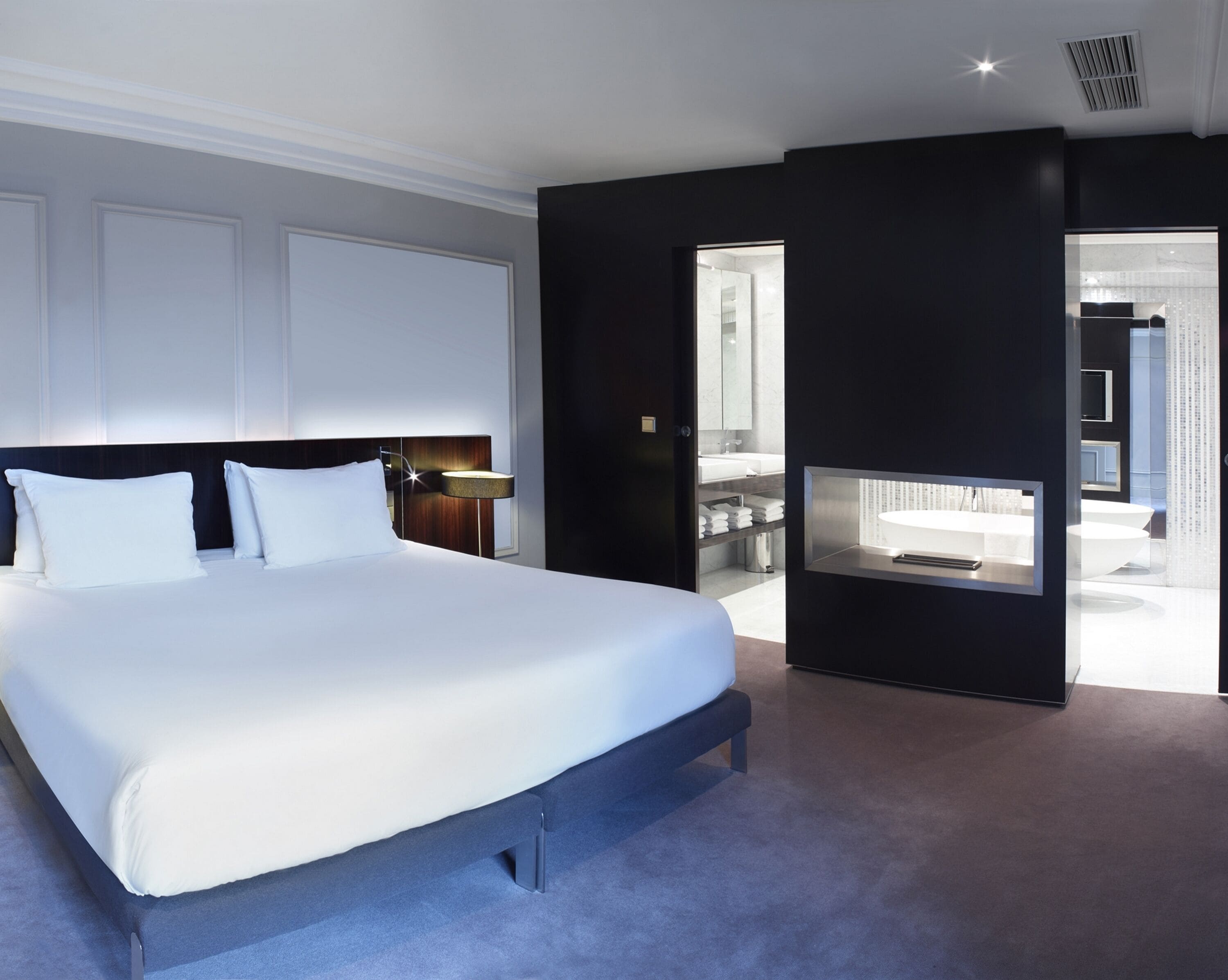 A modern hotel room with a large bed, a TV, and a view into the bathroom.