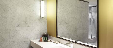 A modern bathroom with a marble wall, a large mirror, a white sink, and a shower area.
