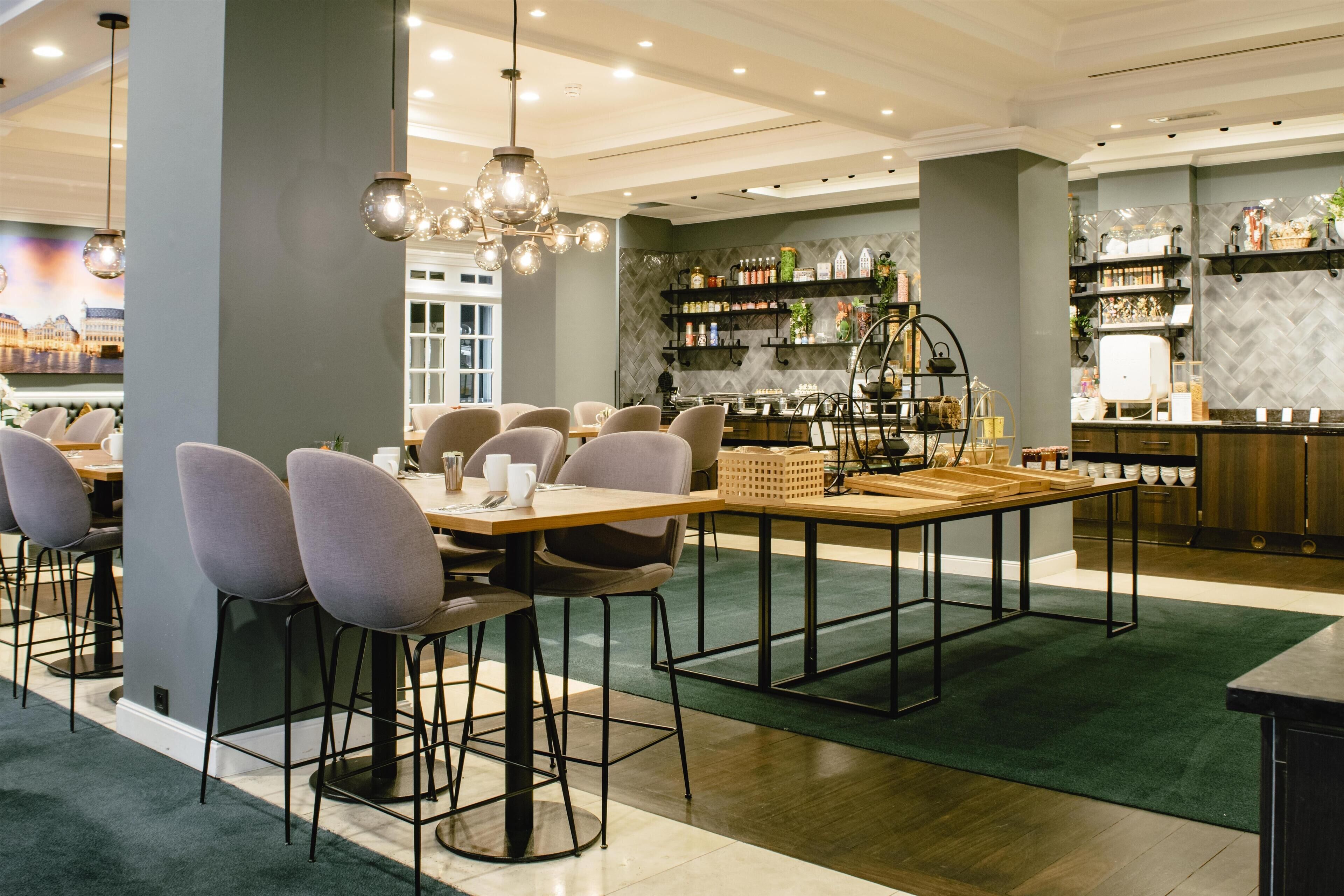 A modern restaurant with a bar area, high chairs, and a variety of shelves stocked with bottles and decorative items.