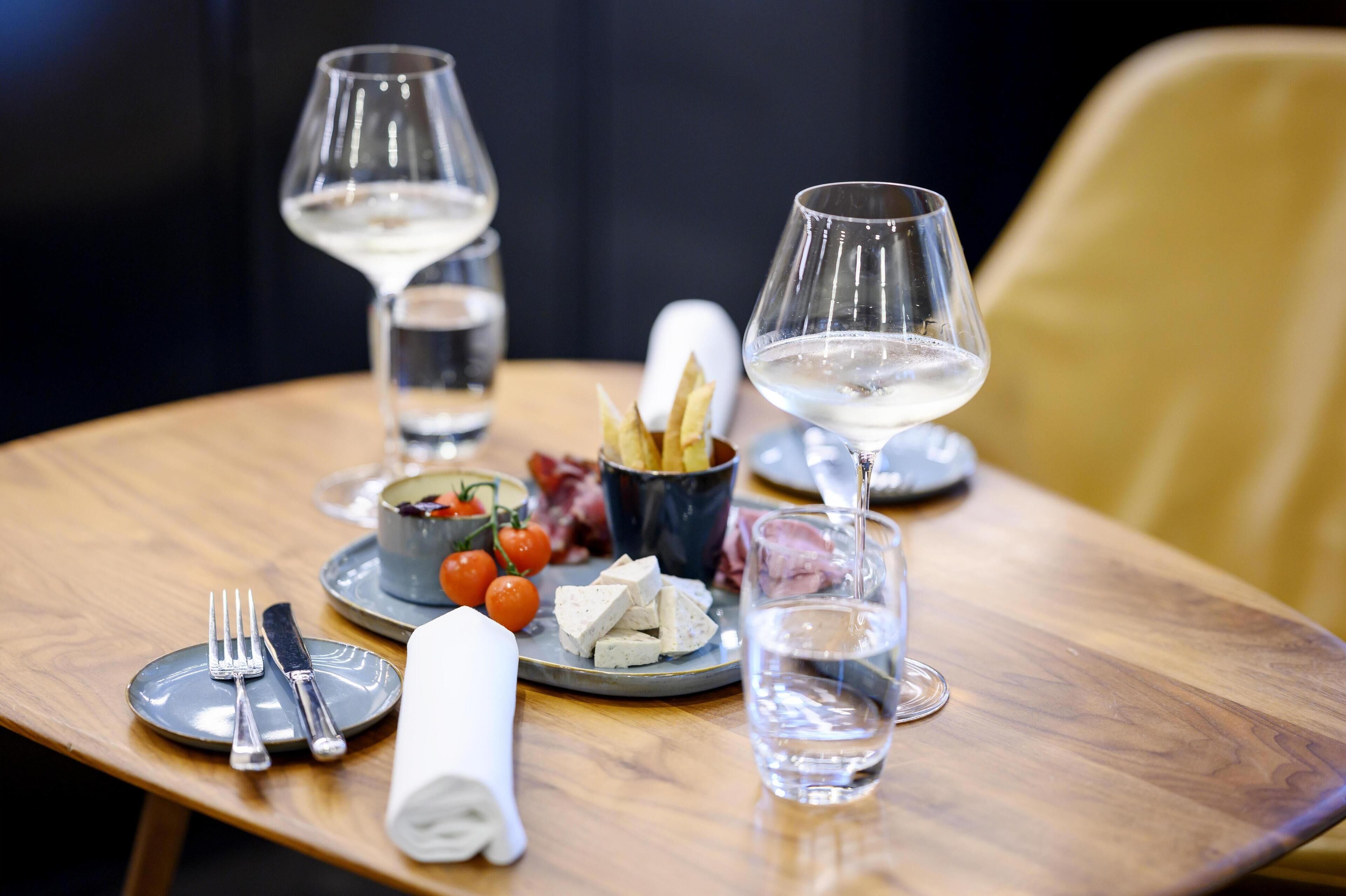 A dining table with a plate of cheese, cherry tomatoes, and breadsticks, accompanied by two glasses of white wine and a glass of water.