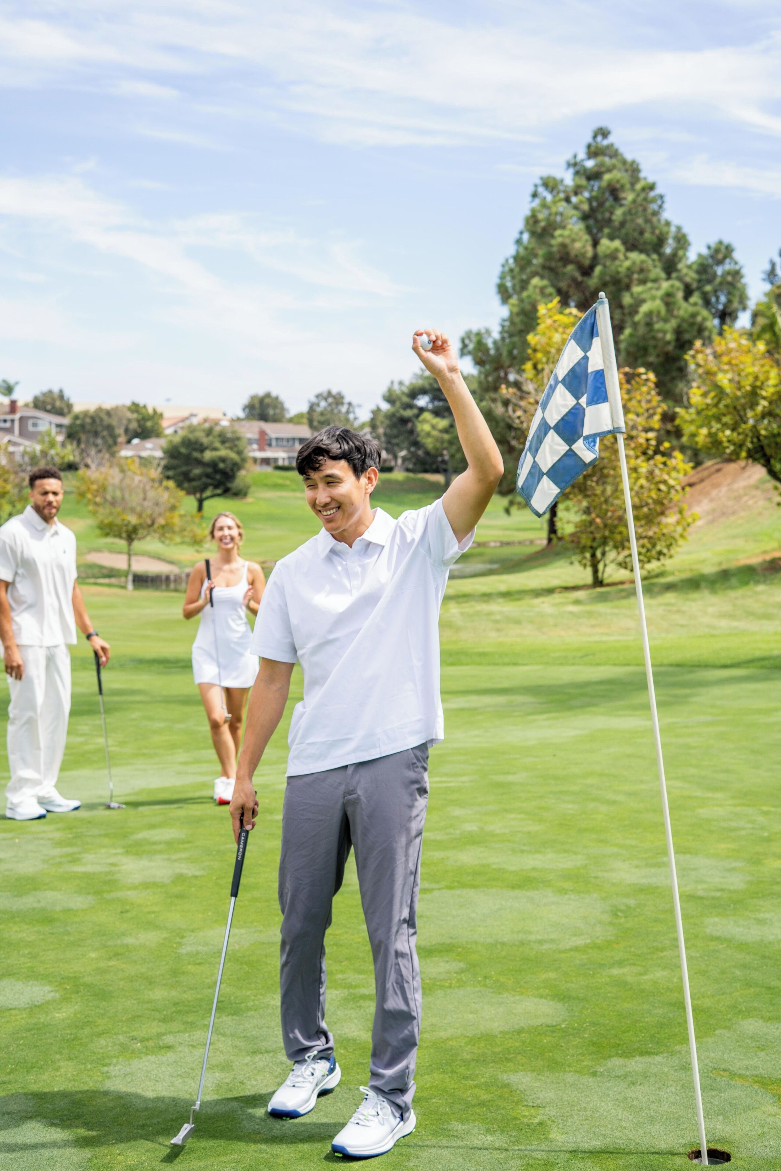 Un campo de golf con una bandera, una persona con camisa blanca y otra con vestido blanco.
