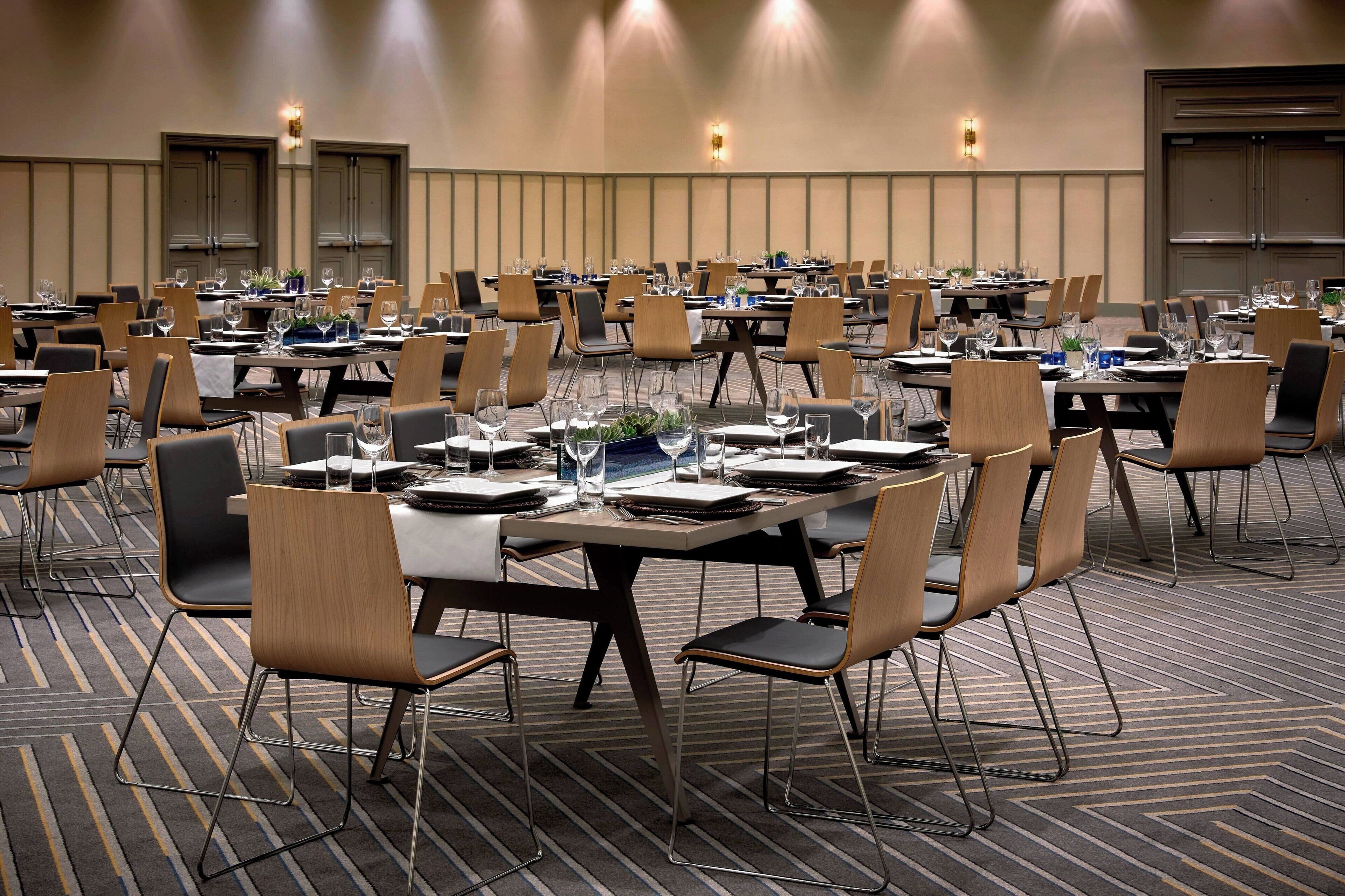 A conference room with multiple tables and chairs, equipped with water glasses, plates, and cutlery.