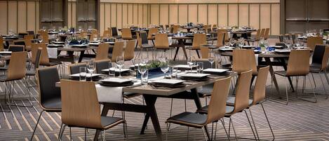 A conference room with multiple tables and chairs, equipped with water glasses, plates, and cutlery.